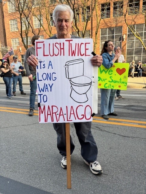 Photo of protestor holding a sign saying Flush Twice, It's a Long Way to Mar-a-Largo