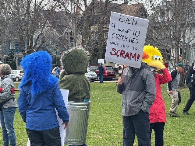 Photo of protester holding sign saying "Even 9 out of 10 grouches want him to scram"